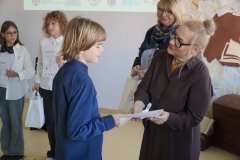 Dyrektor Szkoły Podstawowej nr 22 i przewodnicząca jury wręczają chłopcu dyplom i torbę z logo konkursu, w tle widać innych laureatów