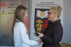 zbliżenie na dwie postacie – kobieta - Dyrektor Szkoły Podstawowej nr 22 wręcza nagrodę Złote Pióro dziewczynce - laureatce
