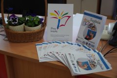 zdjęcie z publikacją, która zawiera fragmenty nagrodzonych archiwalnych prac, na okładce logo konkursu – kolorowe pióro, obok prezentowane są egzemplarzami gazetki uczniowskiej „Szatnia” też z logo konkursu