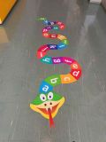 Kolorowa naklejka podłogowa w kształcie uśmiechniętego węża alfabetu. Ciało węża składa się z wielobarwnych pól z kolejnymi literami alfabetu, tworząc krętą ścieżkę do nauki i zabawy na korytarzu.