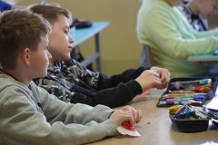 Sala lekcyjna. Uczniowie klasy czwartej siedząc w ławkach, drą na małe kawałki własnoręcznie wykonane serca z papieru.