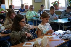 Sala lekcyjna. Uczniowie klasy czwartej siedząc w ławkach, drą na małe kawałki własnoręcznie wykonane serca z papieru.