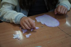Sala lekcyjna. Uczniowie klasy czwartej siedząc w ławkach, próbują skleić podarte na małe kawałki własnoręcznie wykonane serca z papieru.
