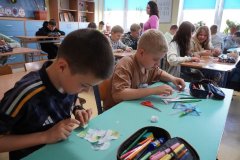 Sala lekcyjna. Uczniowie klasy czwartej siedząc w ławkach, próbują skleić podarte na małe kawałki własnoręcznie wykonane serca z papieru.