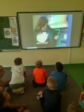 Uczniowie siedzą swobodnie na dywanie i oglądają filmy edukacyjne związane z  rodzajami płatności. 