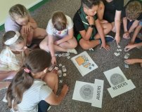 Dzieci siedzą swobodnie na dywanie i wykonują zadania  związane z liczeniem pieniędzy, poznawaniem pojęć awers, rewers.
