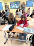 grupa uczniów z klasy 4 siedzi przy stolikach po dwie, cztery osoby i pracuje rysując portret Janusza Korczaka,