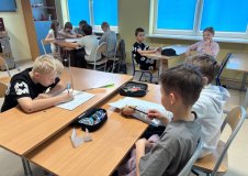 grupa uczniów z klasy 4 siedzi przy stolikach po dwie, cztery osoby i pracuje rysując portret Janusza Korczaka