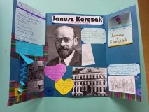 niebieski lapbook z czarnobiałym portretem Korczaka, kolorowymi fiszkami i dwoma serduszkami w kolorze żółtym i różowym