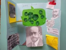 jasnoniebieski lapbook z licznymi obrazkami tematycznie nawiązującymi do patrona szkoły, kolorowymi kopertami