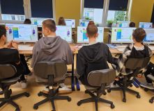 Dzieci przy biurkach z komputerami, uczą się i współpracują w klasie.