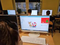 Grupa osób pracujących na komputerach w klasie, skupionych na zadaniach edukacyjnych.