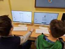 Grupa osób pracujących na komputerach w klasie, skupionych na zadaniach edukacyjnych.