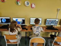 Dzieci przy biurkach z komputerami, uczą się i współpracują w klasie.