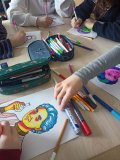 blat stołu, dłonie uczniów, szkolne piórniki i kolorowe portrety Skłodowskiej w stylu popart