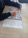blat stołu w szkolnej czytelni, widok na dłonie ucznia i krzyżówka w formacie A3, która uczeń rozwiązuje