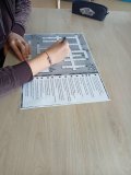 blat stołu w szkolnej czytelni, widok na dłonie ucznia i krzyżówka w formacie A3, która uczeń rozwiązuje