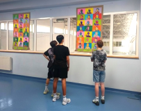 hol przed biblioteką, troje uczniów ogląda kolorową wystawę porterów Marii Skłodowskiej-Curie w stylu popart.