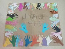 Plakat na szarym papierze z kolorowymi szablonami dłoni uczniów i napisem "W 	grupie siła".