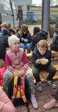 Chłopiec siedzący na ławeczce, trzymający w ręku miskę gorącej grochówki.