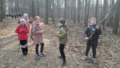 Czworo dzieci na leśnej ścieżce. W tle las i oddalająca się grupa pieszych.