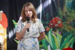 Nauczycielka na tle dekoracji zapowiada przedstawienie w języku angielskim pt. „ Little Red Riding Hood”, czyli „Czerwony Kapturek”
