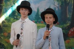 Dwaj uczniowie w czarnych cylindrach na głowie i kolorowych krawatach pełnią funkcję narratorów.
