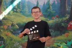 Uczeń z klapsem filmowym zapowiada kolejną scenę bajki.