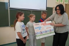 Wicedyrektor Iwona Kołodziejka wręcza trójce uczniów klasy 2b  tablicę pamiątkową. 