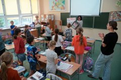 Uczniowie klasy 2b stoją przy ławkach, a przed nimi, przy tablicy stoi pani Iwona Kołodziejksa - wicedyrektor szkoły i gratuluje wygranej. W rękach trzyma podziękowania oraz duże pudło. 
