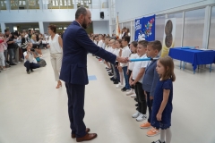 Uczniowie klas pierwszych stojąc na tle napisu Witaj szkoło zostają uroczyście pasowani na pierwszaków przez dyrekcję szkoły, wychowawców, nauczycieli i zaproszonych gości.
