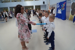 Uczniowie klas pierwszych stojąc na tle napisu Witaj szkoło zostają uroczyście pasowani na pierwszaków przez dyrekcję szkoły, wychowawców, nauczycieli i zaproszonych gości.