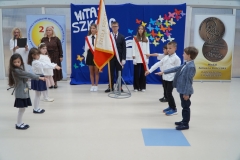 Wybrani przedstawiciele klas pierwszych w strojach galowych na tle napisu Witaj szkoło uroczyście wygłaszają tekst ślubowania.