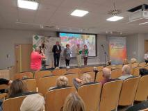 Aktorzy Teatru Remedium SUTW podczas prezentacji fragmentów nagrodzonych opowiadań. W tle zdjęcia z pobytu Seniorów w naszej Szkole w czerwcu 2023 roku podczas realizacji projektu „SENIORZY CZYTAJĄ MŁODZIEŻY”.
