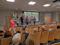 Aktorzy Teatru Remedium SUTW podczas prezentacji fragmentów nagrodzonych opowiadań. W tle zdjęcia z pobytu Seniorów w naszej Szkole w czerwcu 2023 roku podczas realizacji projektu „SENIORZY CZYTAJĄ MŁODZIEŻY”.