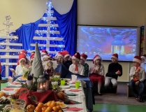 Odświętnie udekorowana sala  lekcyjna, stół wigilijny, w oddali widać siedzące dzieci.