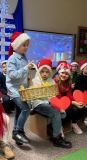 Odświętnie ubrany uczeń z koszyczkiem w dłoni udaje się rozdawać  uczestnikom  spotkania kartki świąteczne.