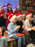 Odświętnie ubrani uczniowie w czapkach Mikołaja śpiewają kolędy.