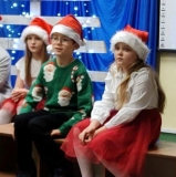 Odświętnie ubrani uczniowie w czapkach Mikołaja śpiewają kolędy.