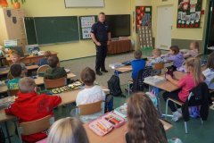 (sala lekcyjna) Uczniowie klasy pierwszej, siedząc w ławkach, słuchają zaproszonego gościa- asp. Krzysztofa Czarnomskiego, dzielnicowego z Komendy Miejskiej Policji w Płocku i odpowiadają na jego pytania.