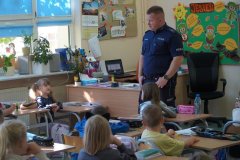 (sala lekcyjna) Uczniowie klasy pierwszej, siedząc w ławkach, słuchają zaproszonego gościa- asp. Krzysztofa Czarnomskiego, dzielnicowego z Komendy Miejskiej Policji w Płocku i odpowiadają na jego pytania.