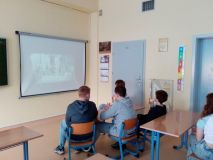 grupa uczniów siedzi w ławkach w sali lekcyjnej i na dużym ekranie ogląda projekcję filmu 