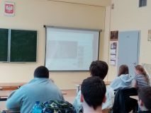 grupa uczniów w sali lekcyjnej ogląda projekcję filmu na dużym ekranie