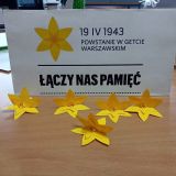 papierowe żonkile – symbol powstania żydowskiego leżą na blacie ławki w tle napis „19.IV.1943 r. Powstanie w getcie warszawskim Łączy nas pamięć.”