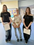 Trzy starsze przedstawicielki SU z teczkami z dokumentami w rękach oraz koszem lizaków od Rady Rodziców i własnoręcznie zrobionymi medalami dla „Najsympatyczniejszych Chłopaków wklasie”. Wszystkie uczennice są pogodne.