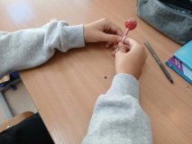 Zbliżenie na ławkę szkolną i ręce jednego z uczniów, który trzyma lizaka od Rady Rodziców.