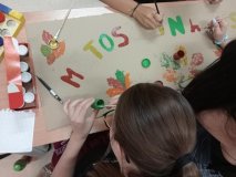 Uczestniczki Koła Samorządu Uczniowskiego przygotowują baner z prostokoątnego kartonu, na którym farbami  kolorują nakreślony ołówkiem napis: "miętoszki na jesień".