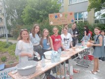 Stoisko złożone z ławek, a na nim mnóstwo mąki, miski, buteli i balony, z których kilkoro uczestników Koła wraz z nauczycielką wykonują gniotki dla uczestników Festynu Rodzinnego, który odbwa się przed szkołą