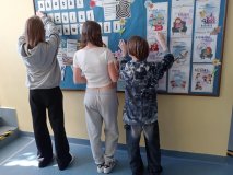 Troje uczestników koła- przywieszają gazetki (o tematyce niskiej frekwencji szkolnej oraz sposobach efektywnej nauki) na tablicy Samorządu Uczniowskiego, która znajduje sie na szkolnym korytarzu