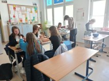 Uczniowie pracujący w grupach podczas przygotowywnia materiałów na Festyn Rodzinny– część wykonuje prace ręczne przy stole, inni przygotowują materiały przy oknie. W tle widoczna gazetka szkolna oraz plansze edukacyjne 